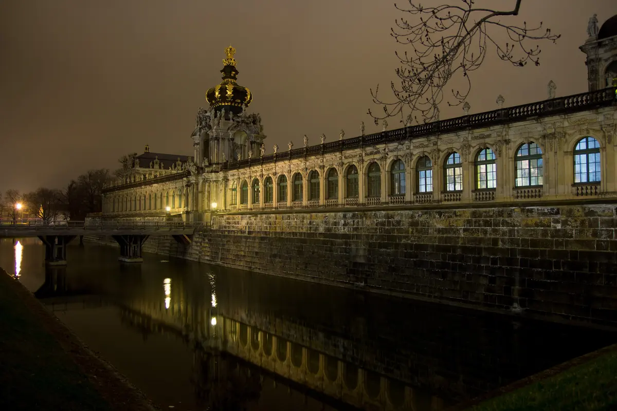 The Crown Gate and the long gallery of the Zwinger at night, with lit windows reflected in the moat.