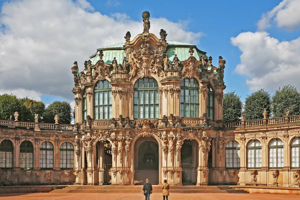 The front of the Wallpavillon in the Dresden Zwinger, with carved stone figures, tall arched windows, a green roof and two curved arcades on either side.